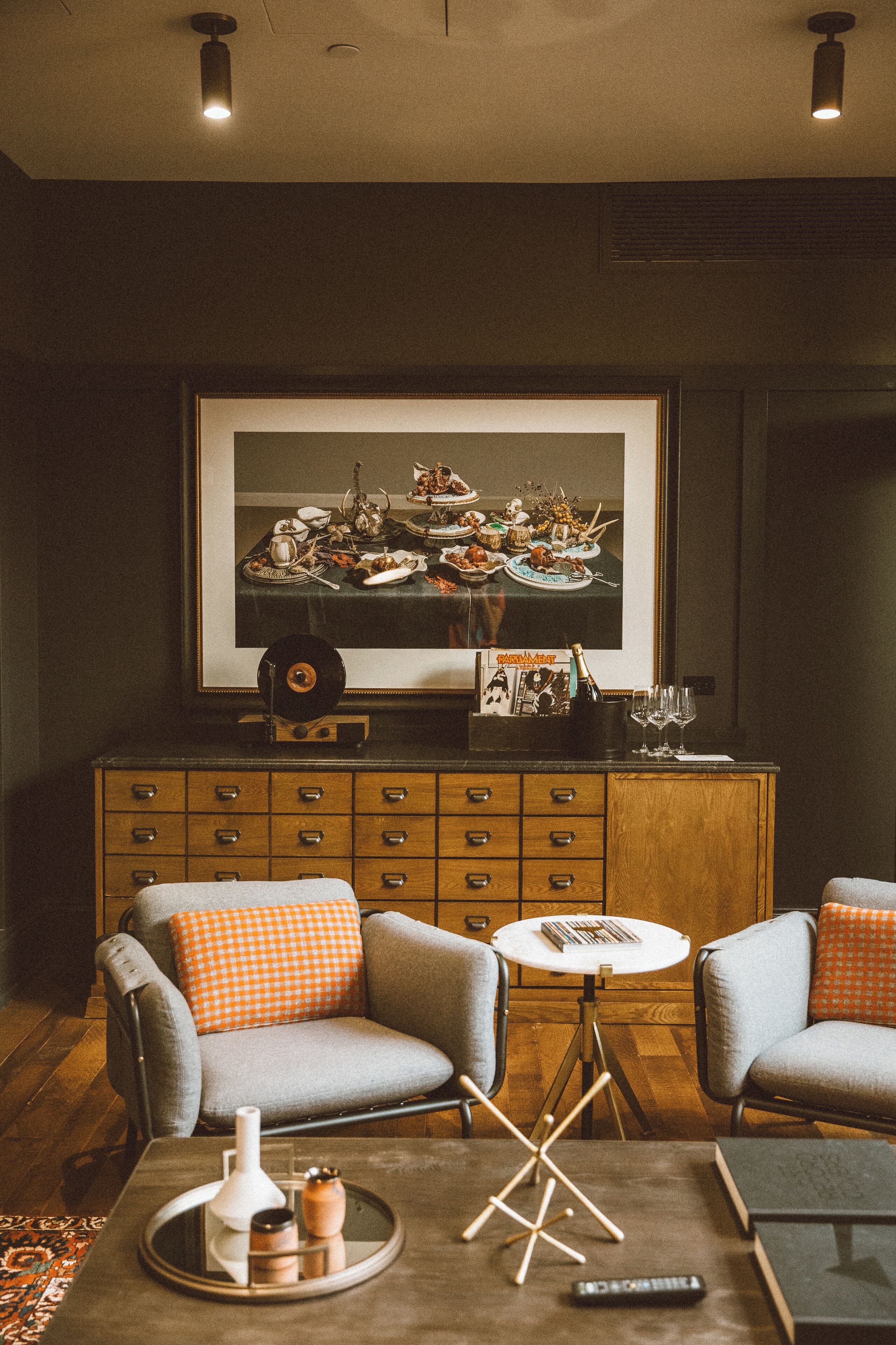 A living room with a large framed picture, two armchairs, a coffee table, and a wooden cabinet.