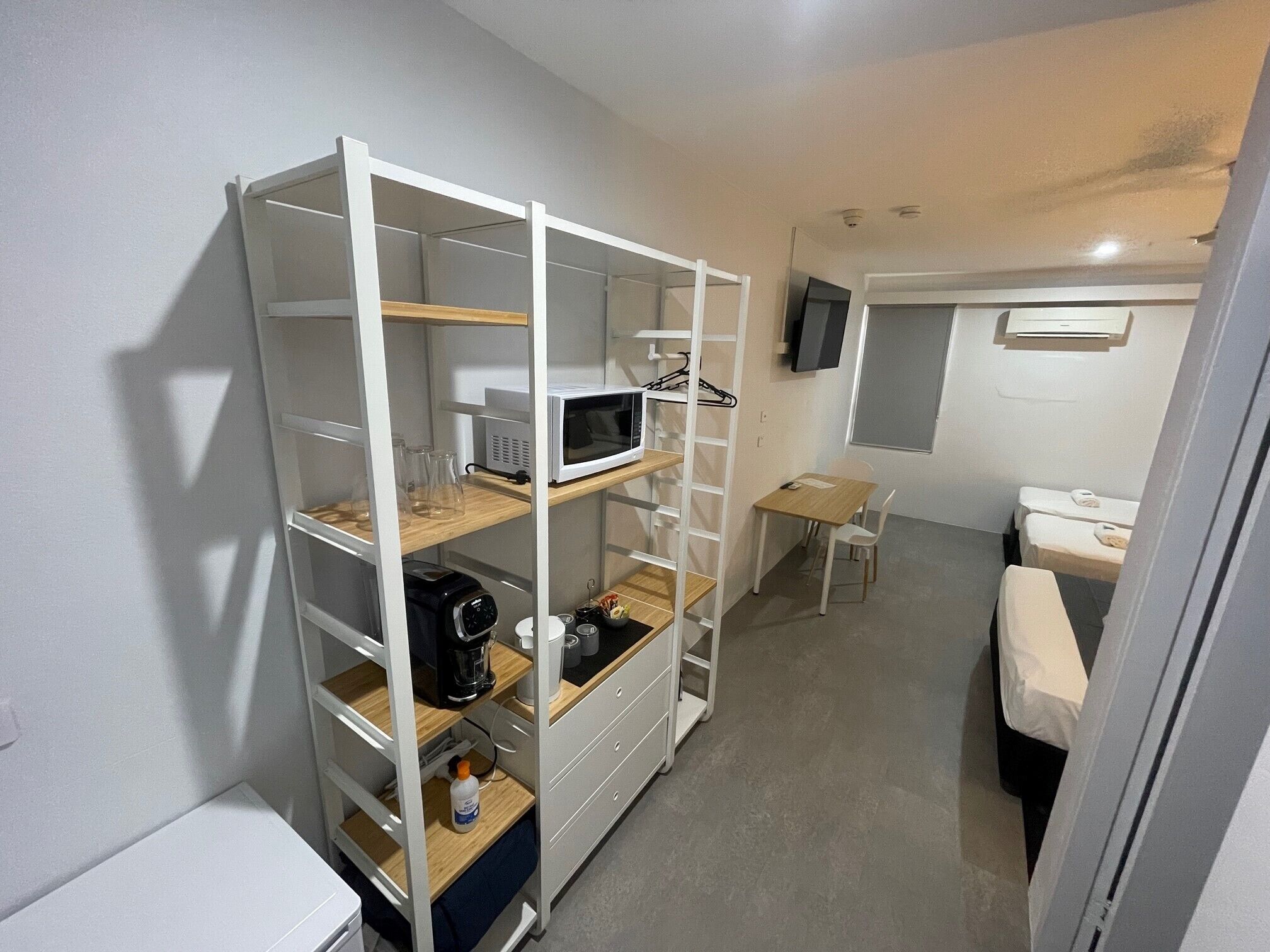 Habitación de hotel pequeña con armario empotrado, un escritorio, una silla, una cama y un televisor fijado a la pared.