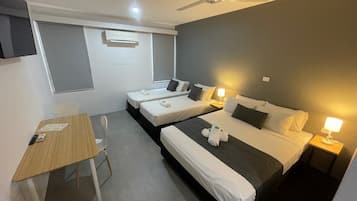A hotel room with two single beds, a desk, a chair, a ceiling fan, and a wall-mounted air conditioner.