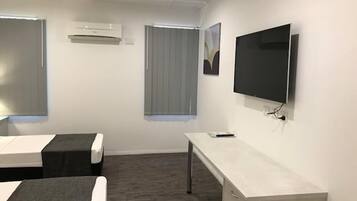 A hotel room with two beds, a desk, a television, and an air conditioning unit.