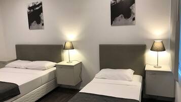 A hotel room with two beds, each with a white mattress and a grey headboard. There are two bedside tables with lamps, and the walls are adorned with black and white artwork.