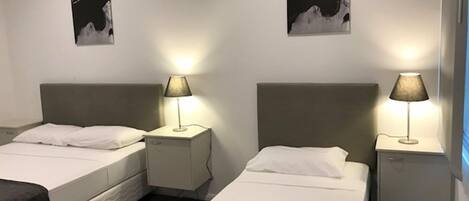 Een hotelkamer met twee bedden, elk voorzien van een wit matras en een grijs hoofdeinde. Er zijn twee nachtkastjes met lampen, en de muren zijn versierd met zwart-wit kunstwerken.