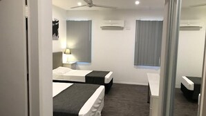 Ein Hotelzimmer mit zwei Betten, einem Deckenventilator, Klimaanlagen, einem Nachttisch mit Lampe und einem Spiegel.