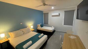 A hotel room with two beds, a desk, and a chair. There is a ceiling fan, an air conditioning unit, and a window.