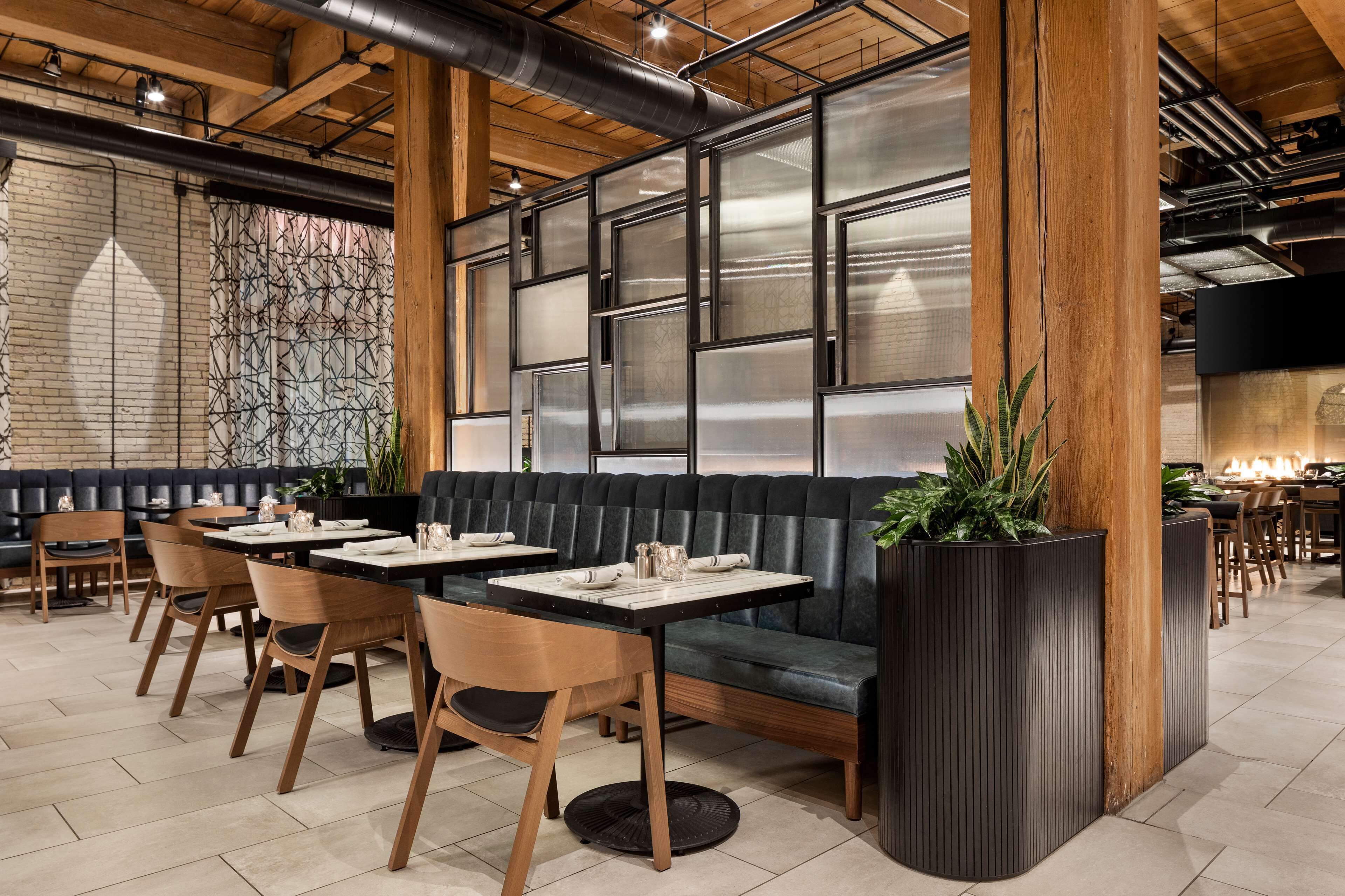 Interior moderno de restaurante con vigas de madera, una banca acolchada negra y un amplio ventanal con marcos metálicos.