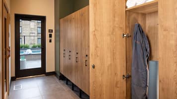 Un pasillo de hotel con taquillas de madera, una puerta que da al exterior y un perchero con toallas.