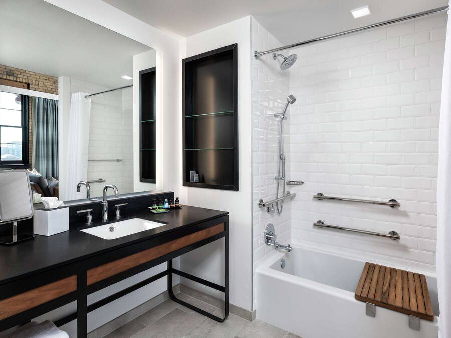 A modern bathroom with a black vanity, a large mirror, a white bathtub, and a shower with a glass door.