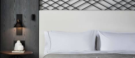 A modern hotel room with a bed, a wooden chair, a small table, and a patterned floor.