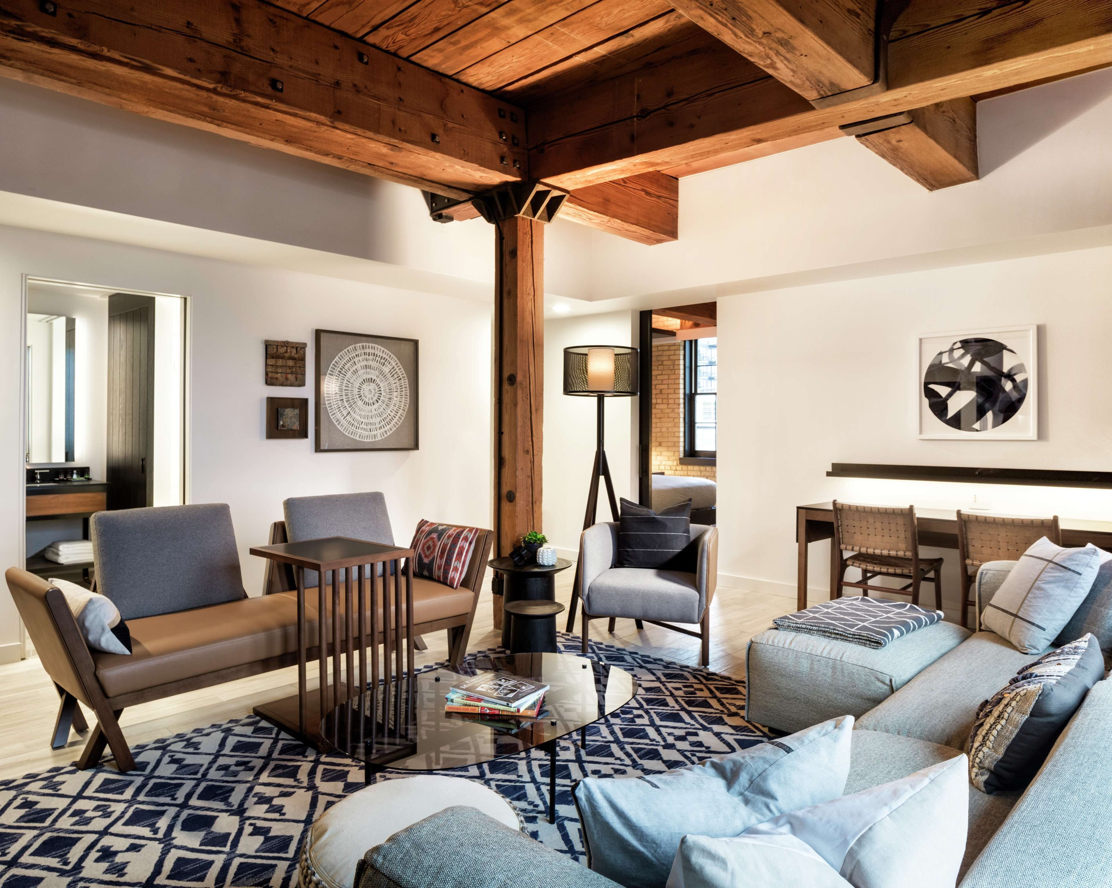 A spacious living room with a high ceiling, wooden beams, a large sofa set, a coffee table, and a dining area with a small table and chairs.