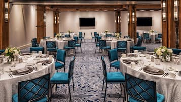 Un salón de banquetes con mesas redondas dispuestas para comer, sillas tapizadas en azul y una alfombra estampada.