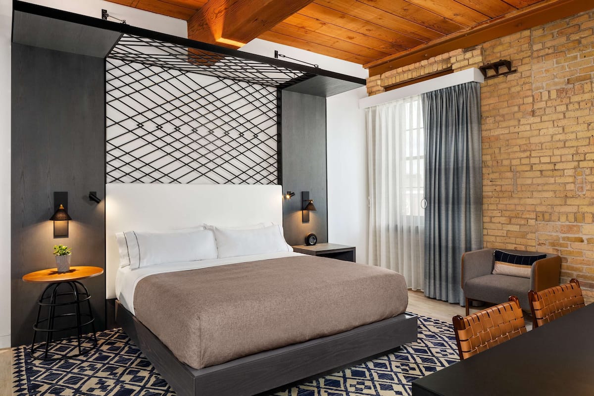 A modern bedroom with a large bed, a small table with a plant, a chair, and a desk with a chair.