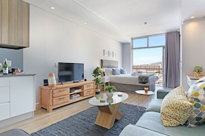 A modern living room with a TV, sofa, and coffee table. There is a balcony with a view of the city.