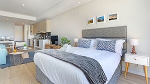 A modern hotel room with a large bed, a desk, a kitchenette, and a bathroom. - Sentinel Luxury Suites (Cape Town)