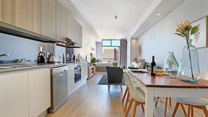 A modern kitchen with a central island, a dining area with a wooden table, and a view of the city through large windows. - Sentinel Luxury Suites (Cape Town)