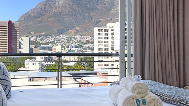 A hotel room with a bed, a view of a mountain, and a cityscape. - Sentinel Luxury Suites (Cape Town)