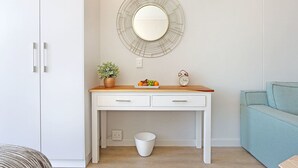 A white desk with drawers, a round mirror with a wireframe frame, a small potted plant, a fruit bowl, and a vintage alarm clock. - Sentinel Luxury Suites (Cape Town)