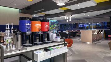Un moderno vestíbulo de hotel con una estación de café, zona de estar y una gran pantalla digital que muestra contenido colorido.