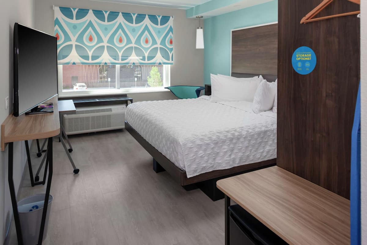 Habitación de hotel con cama, escritorio, silla, televisor y ventana con vistas al exterior, además de un cartel con información sobre opciones de almacenamiento adicionales.