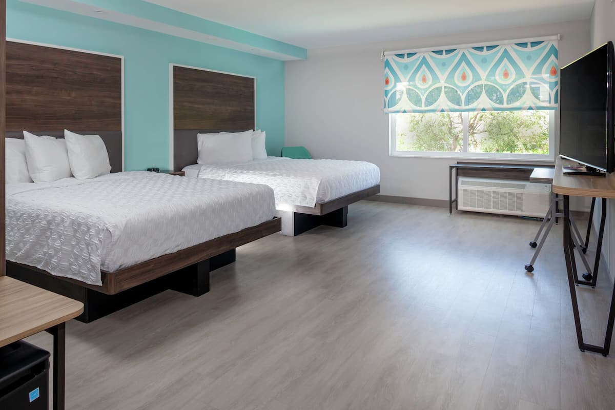 Una habitación de hotel con dos camas, televisión y ventana con cortina estampada.