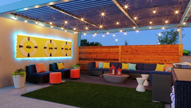 An outdoor patio with a covered seating area, a green artificial turf, and a wooden wall with a yellow sign. - TRU BY Hilton Round Rock (Round Rock)