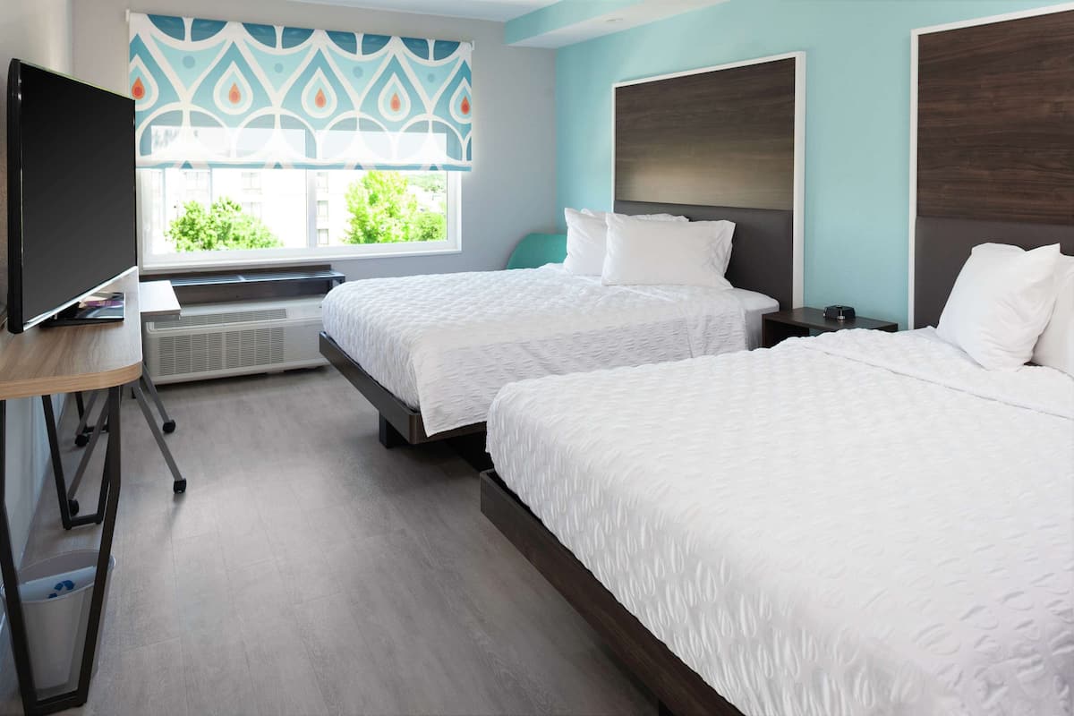 Habitación de hotel con dos camas, televisión, escritorio y ventana con cortinas estampadas.