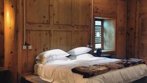 A bedroom with a wooden bed frame, a window with blinds, and a nightstand. - Shangri-La Youyou Inn (Deqin)