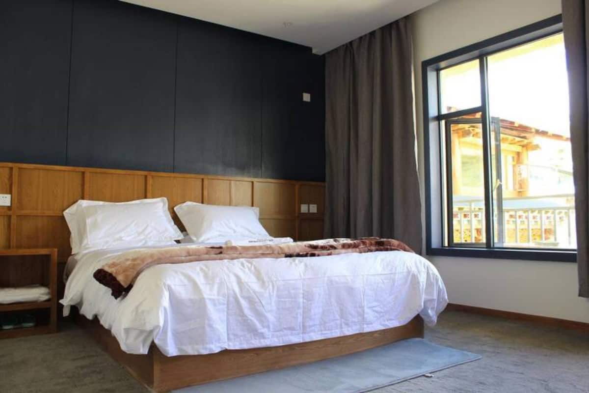 A bedroom with a large bed, wooden headboard, and a window with curtains.