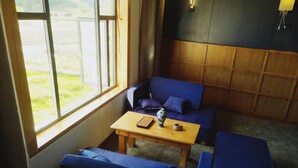 A room with a large window, a blue sofa, a wooden table, and a blue armchair. - Shangri-La Youyou Inn (Deqin)