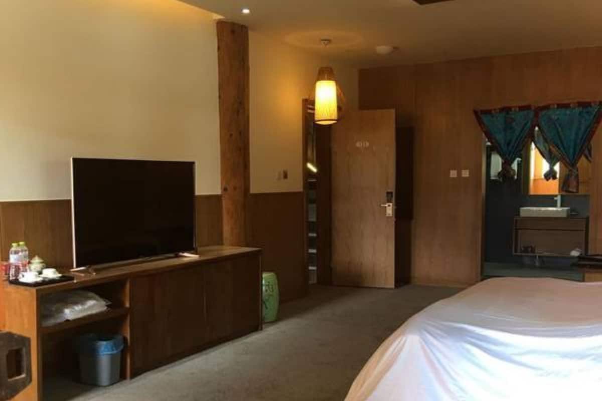 A hotel room with a large bed, a television on a wooden console, a small desk, and a bathroom with a mirror and curtains.