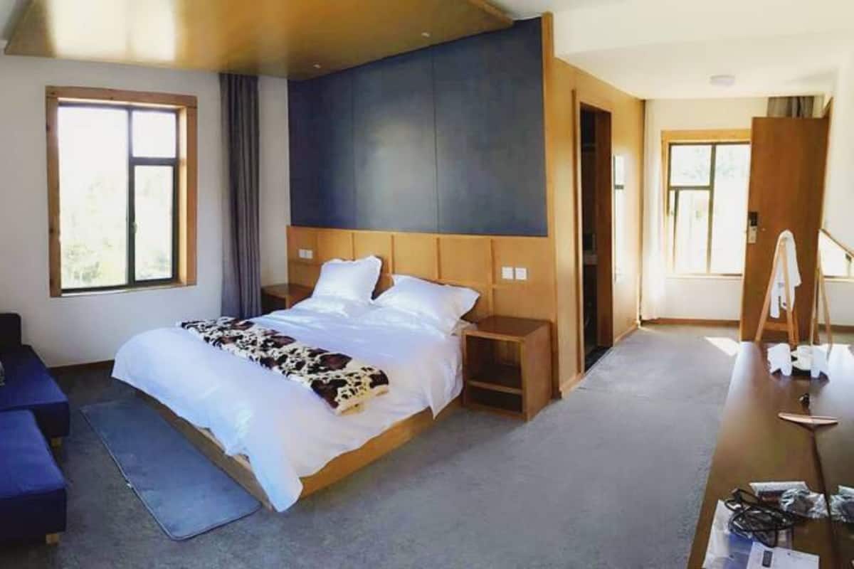 A modern hotel room with a large bed, a desk, a chair, and a view of the outdoors.