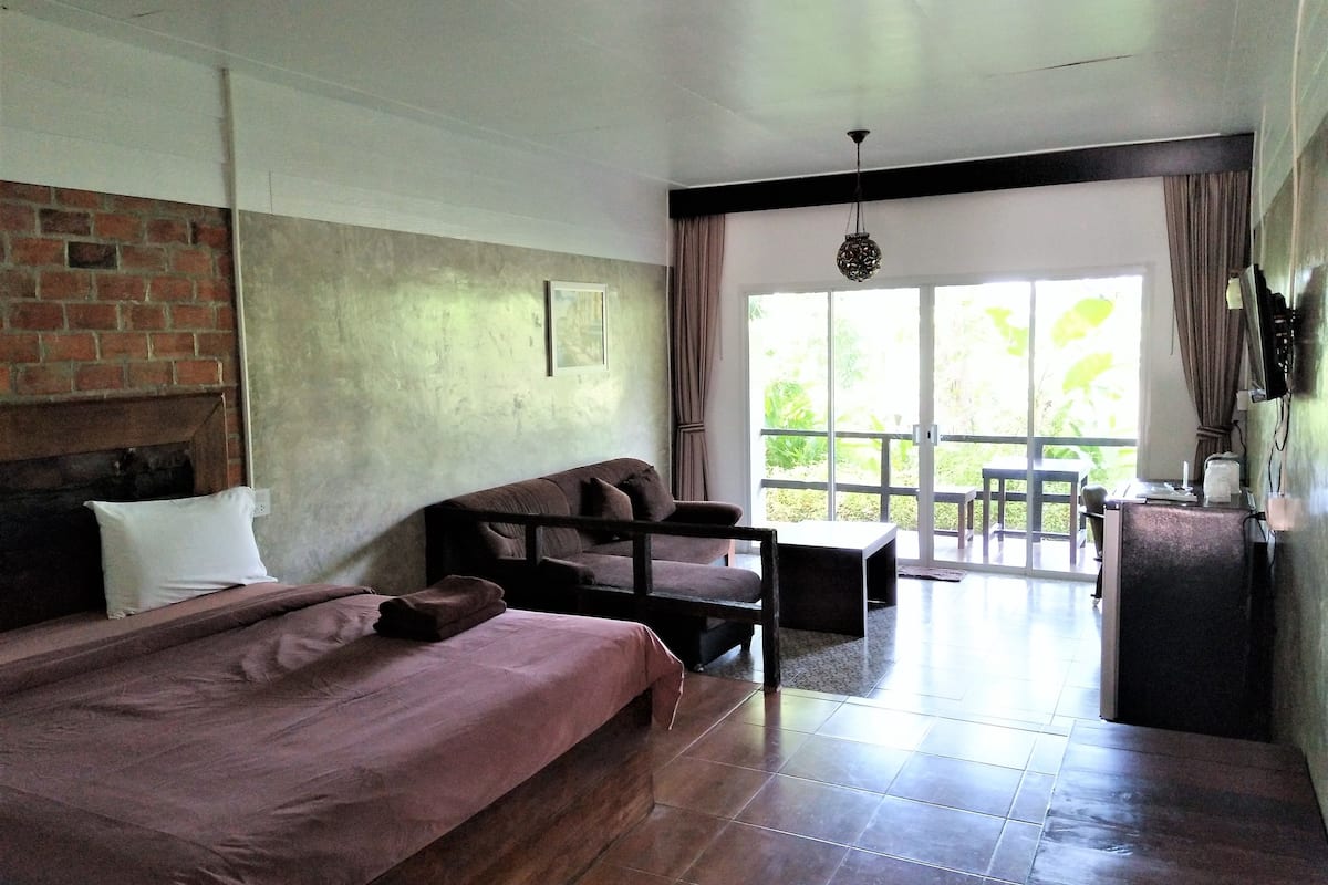 A room with a large bed, a sofa, a desk, and a view of the outdoors.