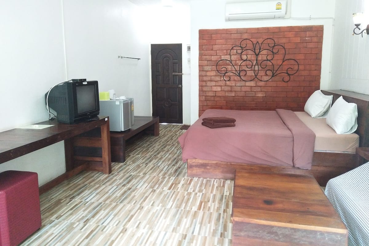 A hotel room with a bed, a desk with a television, a refrigerator, and a brick-patterned headboard.