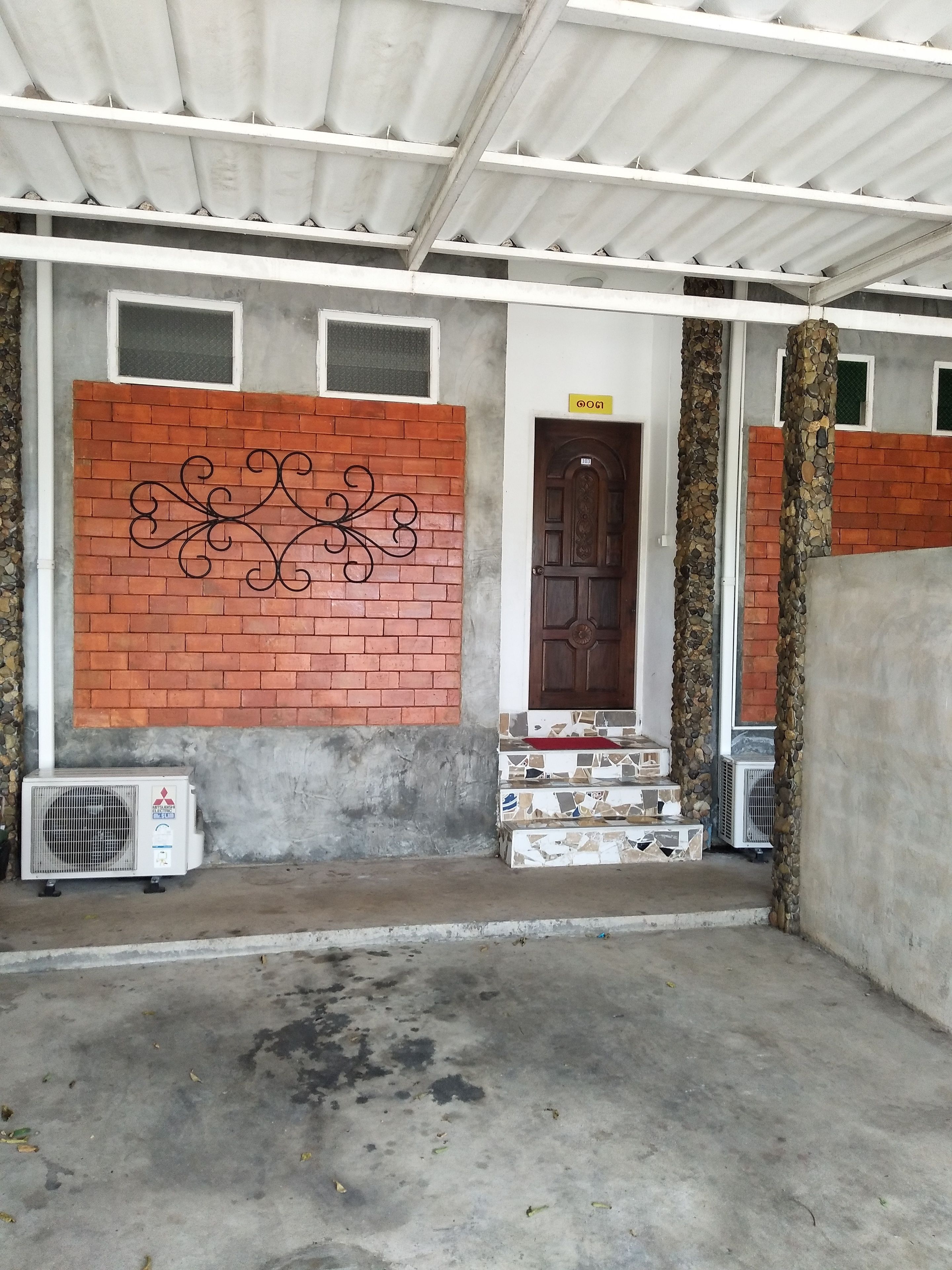 Una entrada de edificio con pared de ladrillo, puerta de madera y unidades de aire acondicionado.