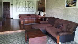Una habitación con un sofá marrón grande, una mesa de centro de madera, una cama con cabecera y un equipo de aire acondicionado de pared.