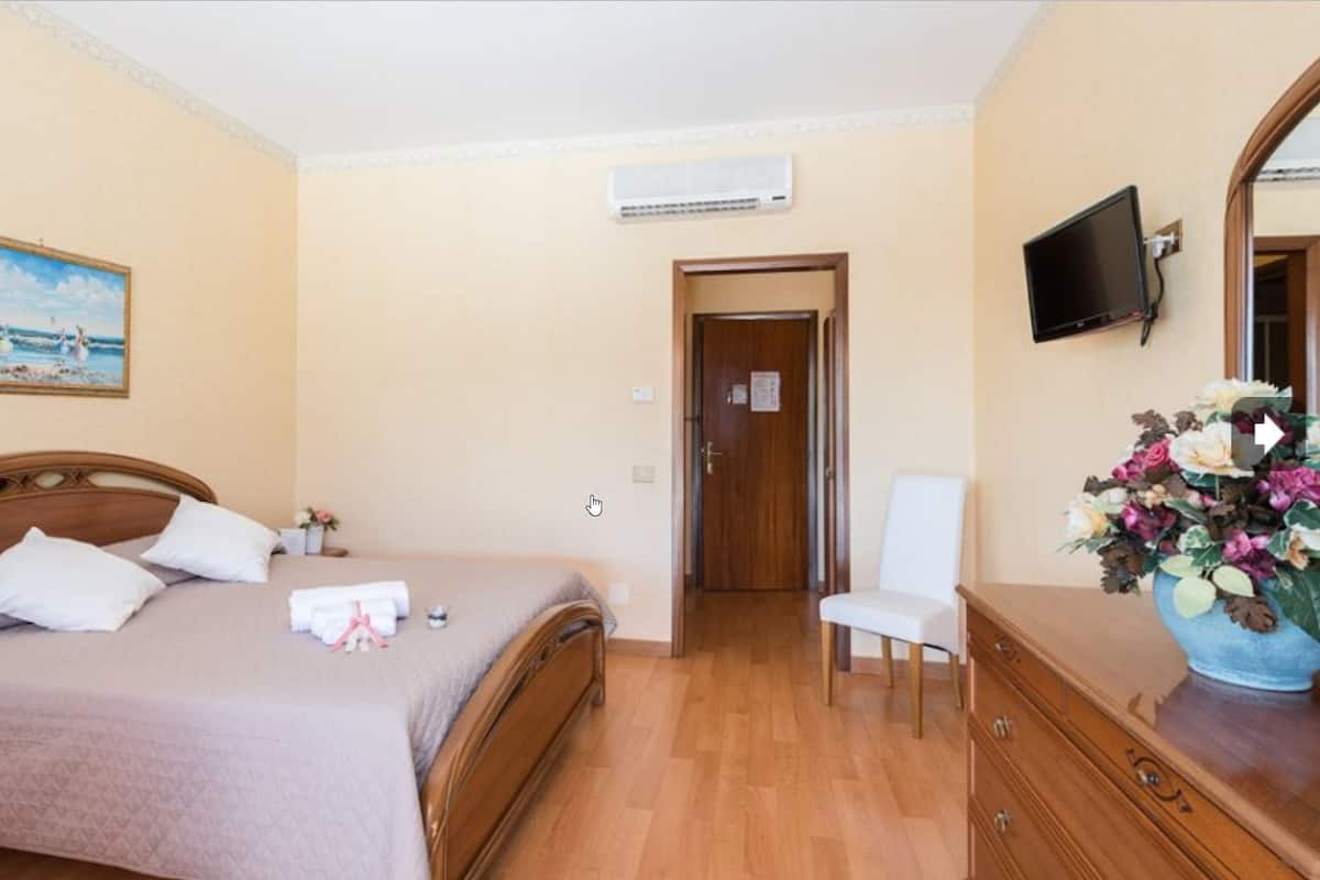 A hotel room with a bed, a chair, a dresser, a TV, and a painting on the wall.