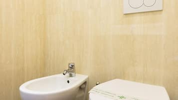 Un baño con un bidé blanco y un inodoro, un perchero de toallas en la pared y un letrero con el símbolo de un inodoro.