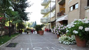 En brostenssti med 'HOTEL CREMONA' malet på, omgivet af plantekasser og udendørs siddeområder.