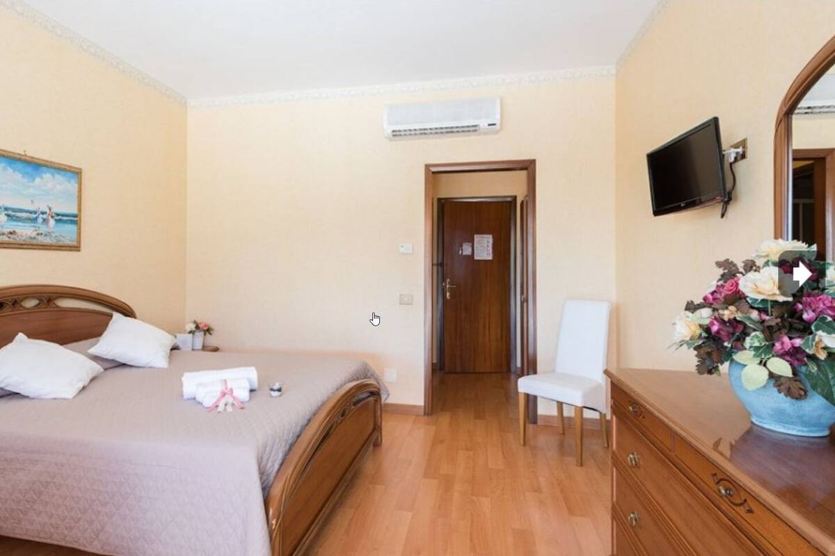 A hotel room with a bed, a chair, a dresser, a TV, and a painting on the wall.