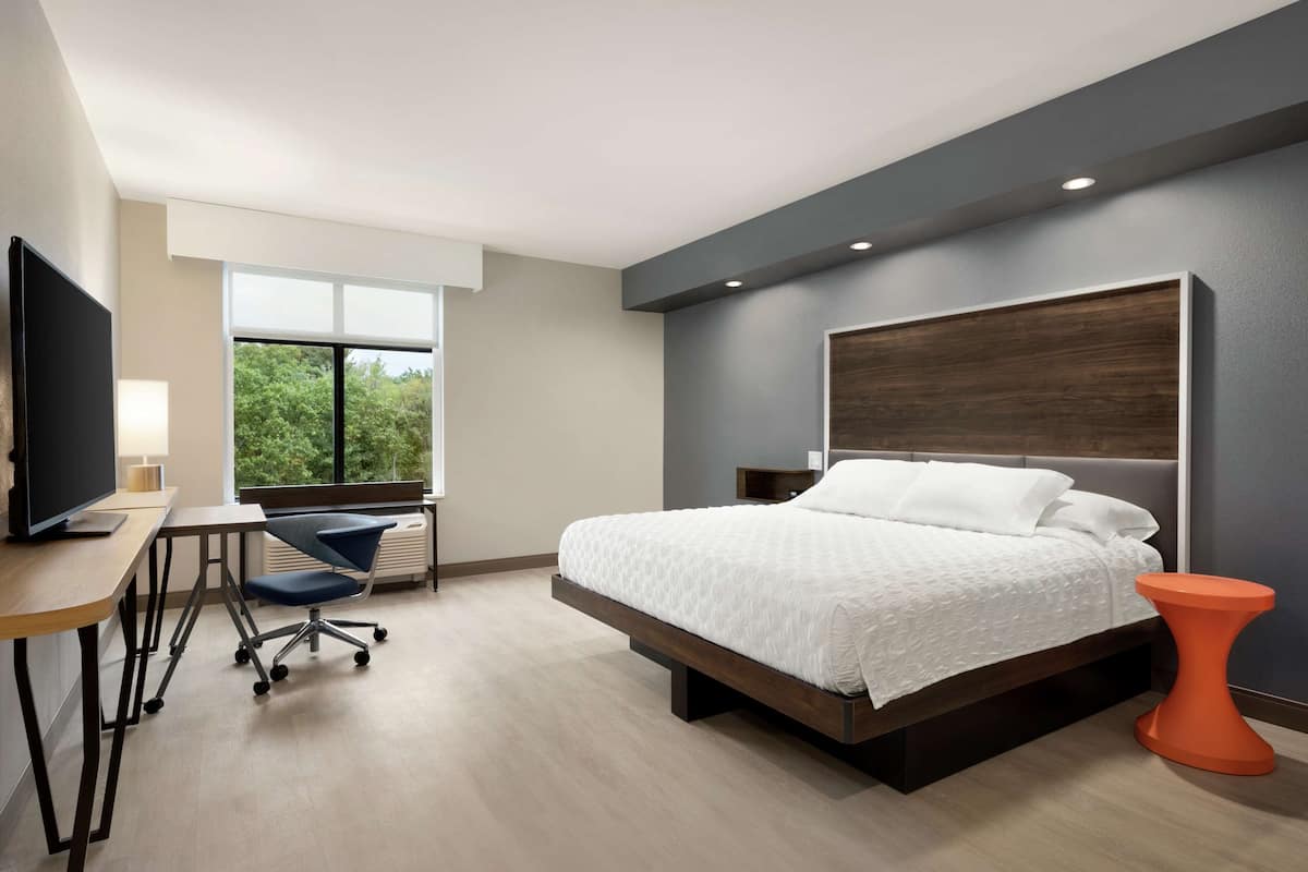 Une chambre d’hôtel moderne dotée d’un grand lit, d’un bureau avec une chaise, d’une télévision et d’une fenêtre donnant sur les arbres.