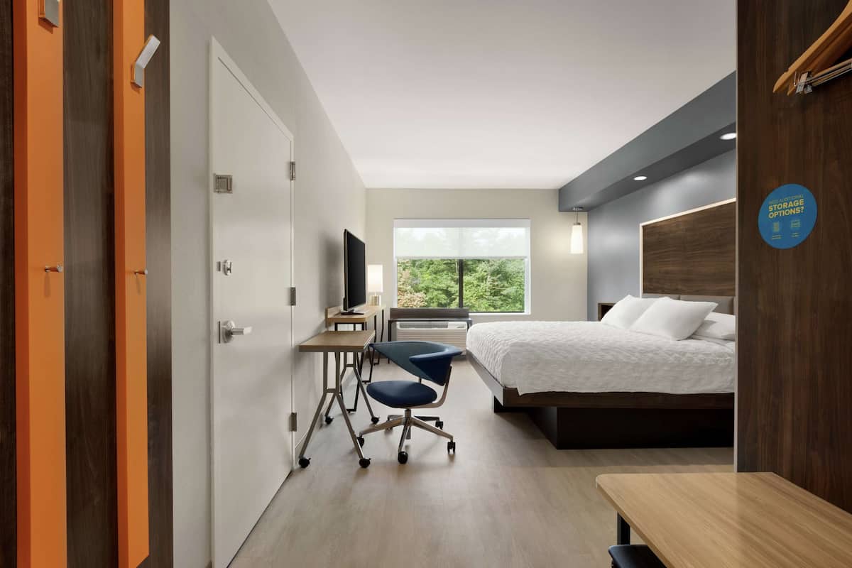 Une chambre d’hôtel équipée d’un lit, d’un bureau, d’une chaise et d’une fenêtre donnant sur un paysage verdoyant.