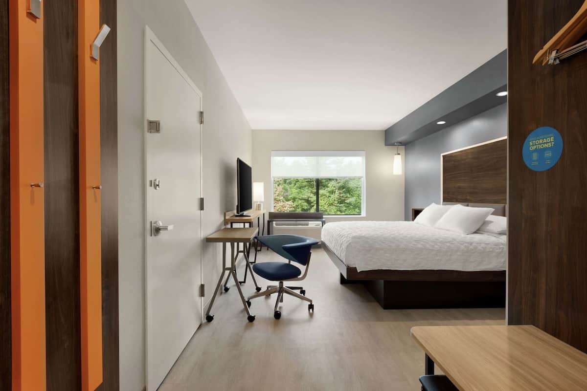 Une chambre d’hôtel équipée d’un lit, d’un bureau, d’une chaise, d’une télévision et d’une fenêtre donnant sur un paysage agréable.