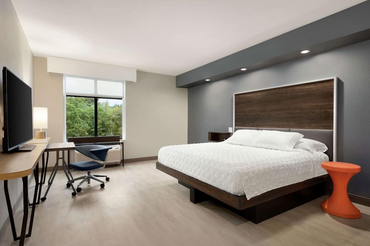 Une chambre d’hôtel moderne équipée d’un lit, d’un bureau, d’une chaise et d’un téléviseur.