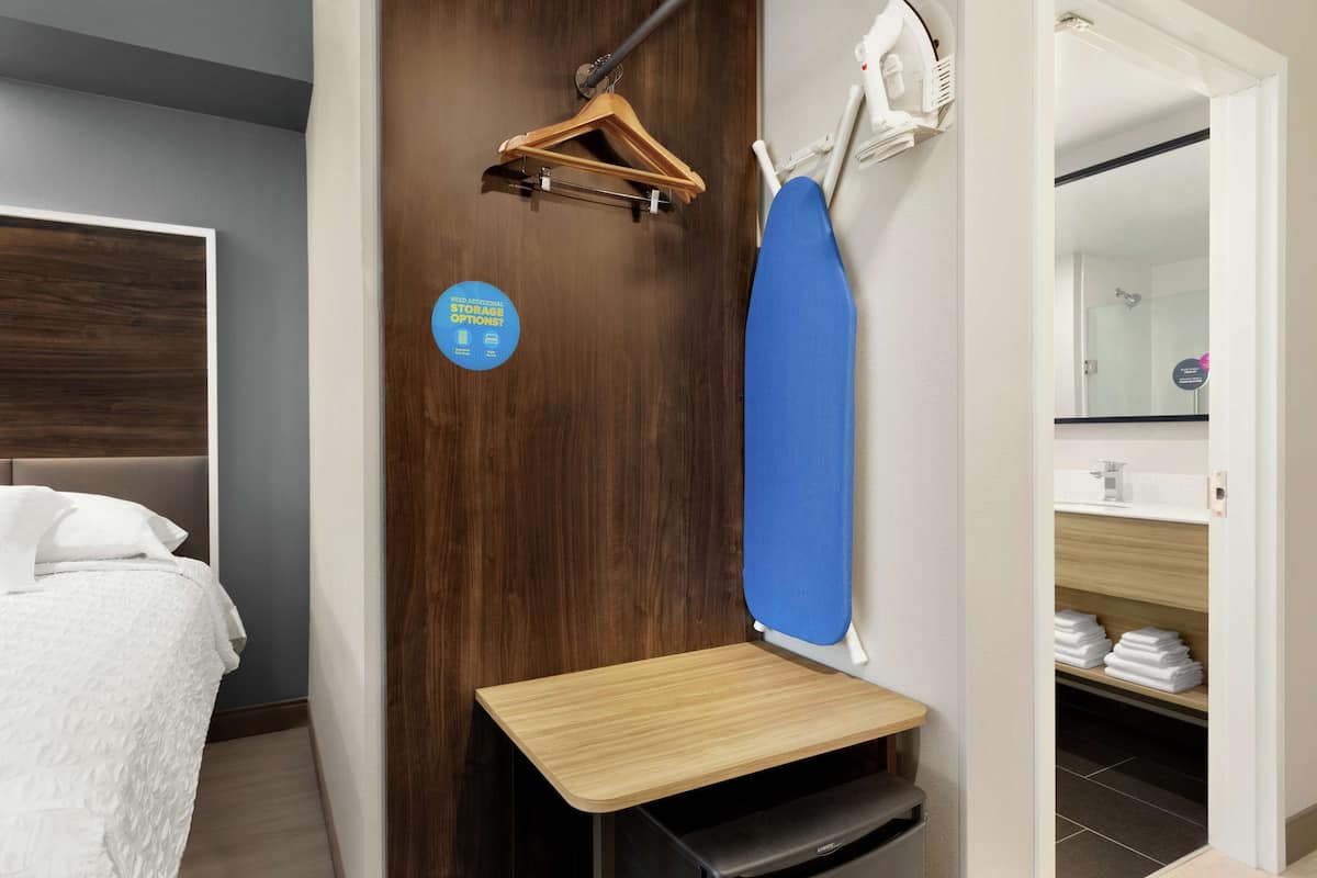 Une chambre d’hôtel avec un lit, une table en bois, un porte-vêtements et une planche à repasser bleue.