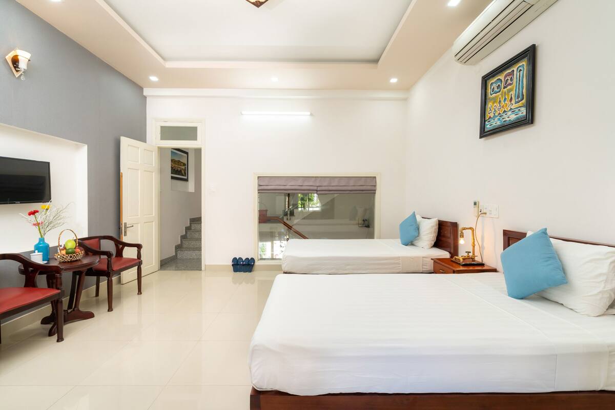 A hotel room with two beds, a TV, a dining table with chairs, and a staircase leading to another room.