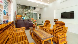 A modern hotel lobby with wooden furniture, a reception desk, a staircase, and a flat-screen TV on the wall. - The Art - Big Sea Villa Hoi An Riverside (Da Nang)