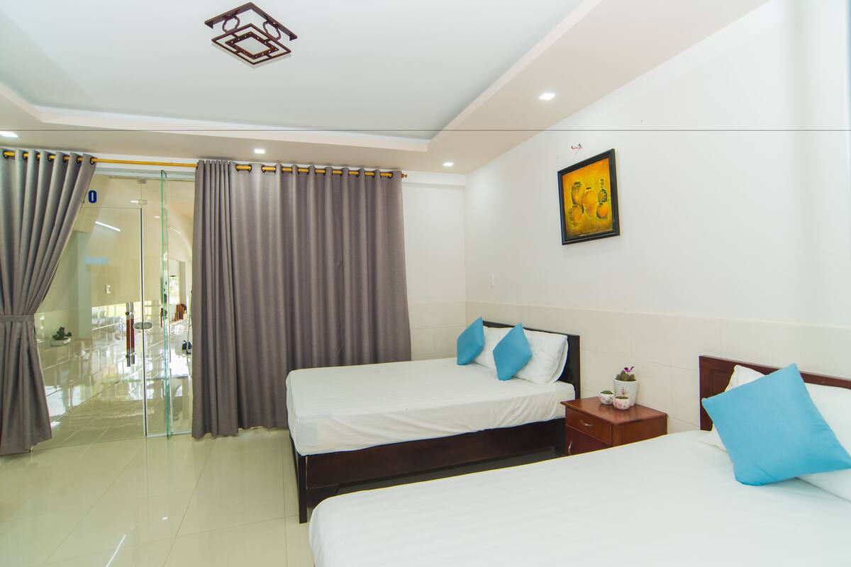 A hotel room with two beds, a glass door entrance, and a painting on the wall.