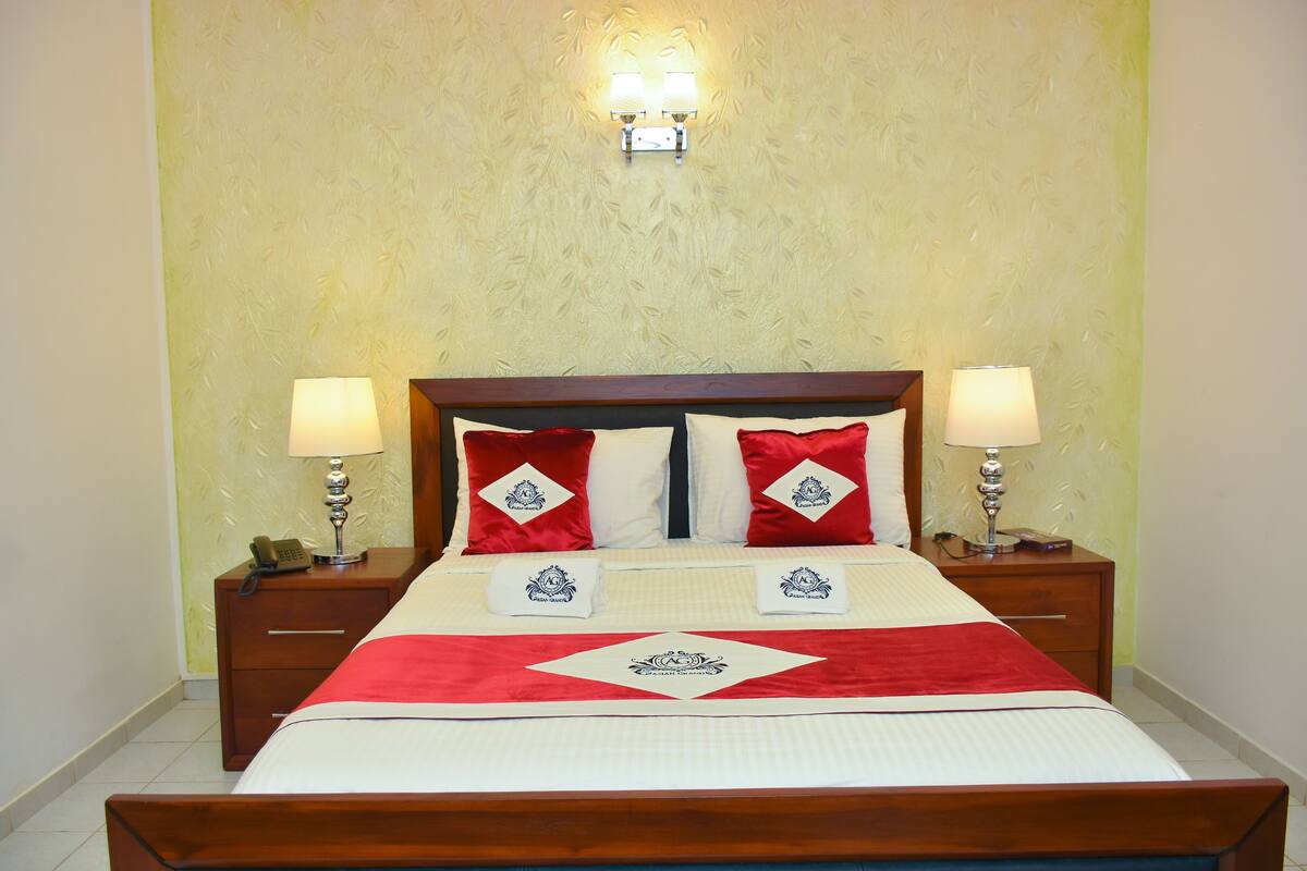 A neatly made bed with a red and white bedspread, two red pillows, and a wooden headboard. There are two bedside tables with lamps and a telephone on one.