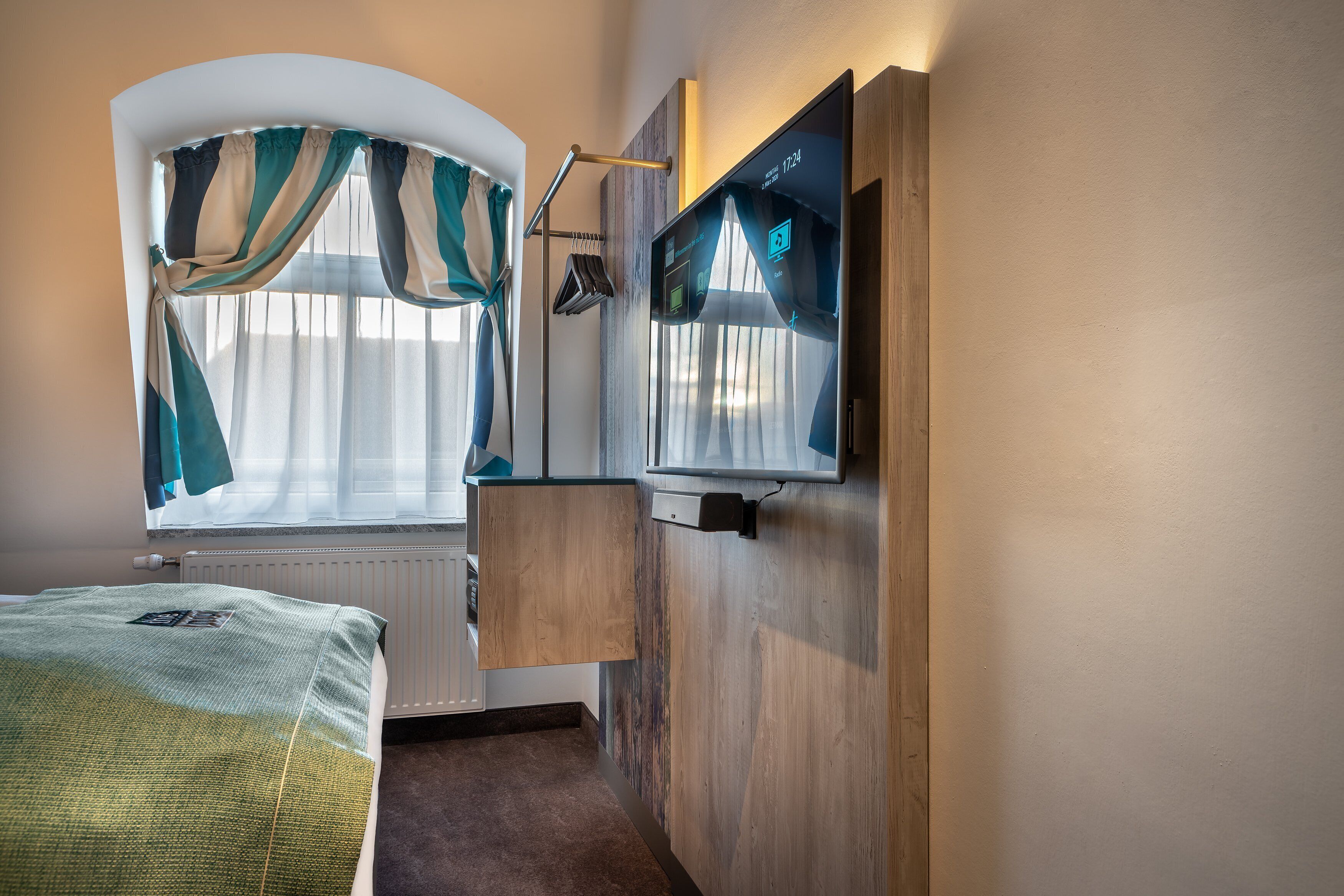 A hotel room with a bed, a window with curtains, a wooden cabinet, and a wall-mounted TV.