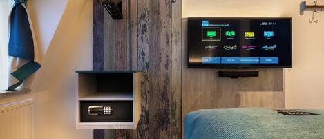 Une chambre d’hôtel moderne dotée d’un téléviseur fixé au mur qui permet de contrôler les différentes fonctions de la chambre, d’un mini-réfrigérateur intégré et d’un mur décoratif en bois.