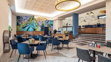A modern hotel lobby with a bar area, seating, and a staircase leading to the upper floor.